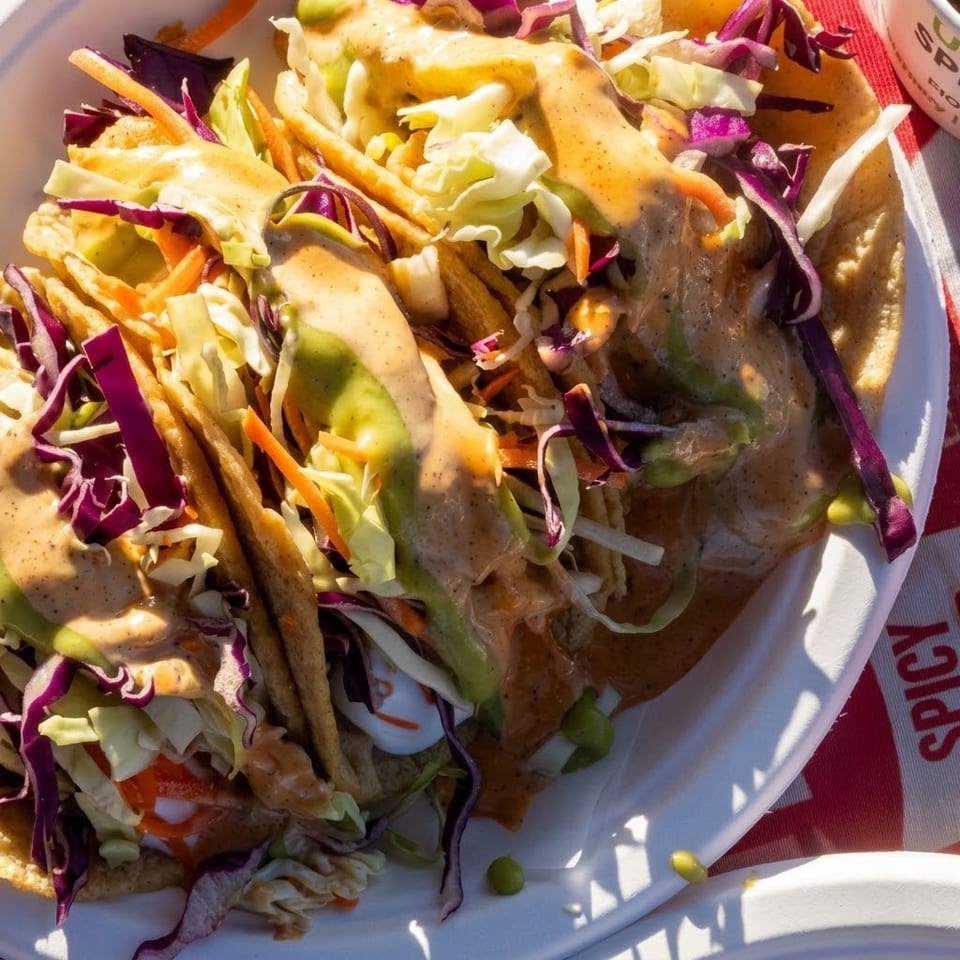 Close-up of crispy tacos filled with grilled fish, shredded cabbage, carrots, avocado, and creamy sauce on a plate.